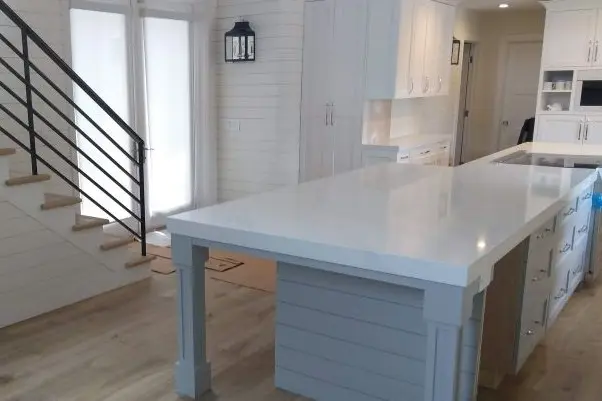 Grey kitchen island with shiplapped staircase and metal railing