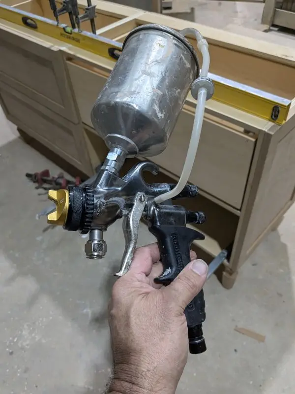 Hand holding a spray gun with a partially finished cabinet in the background